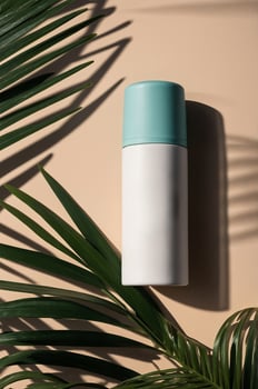 Stylish thermal bottle with teal lid resting on a light background surrounded by tropical leaves photo