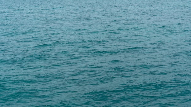 Water of ocean with gentle ripples. Water appears to be a consistent teal or blue green color suggesting a sea or large body of water. Focus is on the water texture and subtle movement. photo