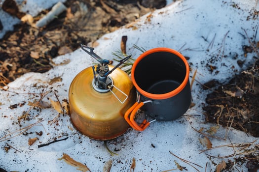 A coffee pot along with a mug is placed on the snowcovered ground, creating a serene winter scene. The contrast of the warm items against the cold snow is quite striking photo