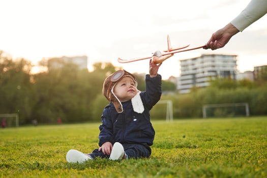 Little boy in aviator glasses is sitting on the field. Woman's hand giving toy plane to him photo