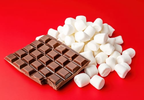 A rich chocolate bar rests beside a pile of fluffy white marshmallows photo