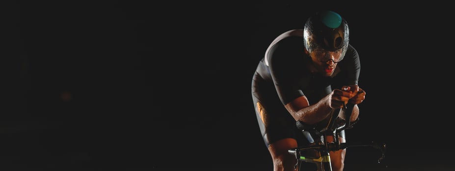 A triathlete rides his bike in the darkness of night, pushing himself to prepare for a marathon. The contrast between the darkness and the light of his bike creates a sense of drama and highlights the photo