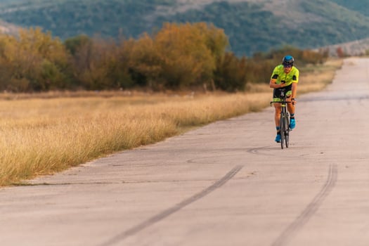 Triathlete riding his bicycle during sunset, preparing for a marathon. The warm colors of the sky provide a beautiful backdrop for his determined and focused effort. photo