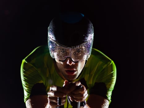 A triathlete rides his bike in the darkness of night, pushing himself to prepare for a marathon. The contrast between the darkness and the light of his bike creates a sense of drama and highlights the photo