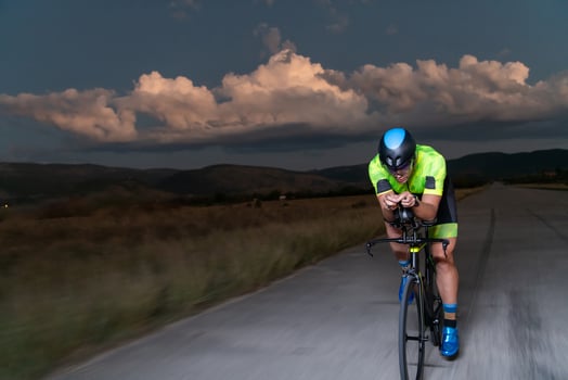 A triathlete rides his bike in the darkness of night, pushing himself to prepare for a marathon. The contrast between the darkness and the light of his bike creates a sense of drama and highlights the photo
