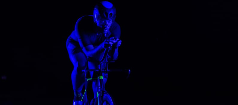 A triathlete rides his bike in the darkness of night, pushing himself to prepare for a marathon. The contrast between the darkness and the light of his bike creates a sense of drama and highlights the photo