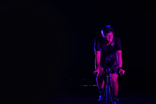 A triathlete rides his bike in the darkness of night, pushing himself to prepare for a marathon. The contrast between the darkness and the light of his bike creates a sense of drama and highlights the photo