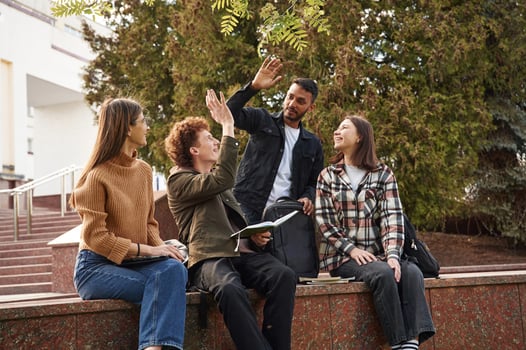 Doing high five. Four young students in casual clothes are together outdoors photo