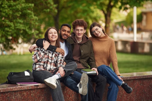 Sitting and smiling... Four young students in casual clothes are together outdoors photo