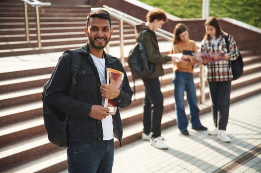 Indian man, is standing in front,, of his friends. Four young students in casual clothes are together outdoors photo