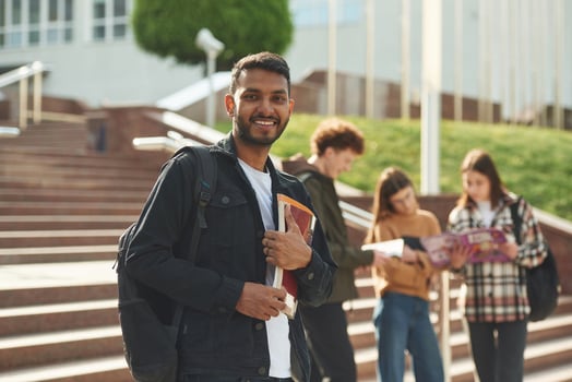 Indian, man, is standing in front of his friends. Four young students in casual clothes are together outdoors photo