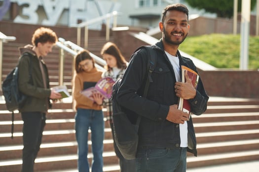 Indian man, is ,standing in front, of his friends. Four young students in casual clothes are together outdoors photo