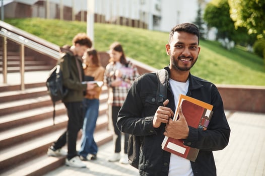 Indian, man is standing in front of his friends. Four young students in casual clothes are together outdoors photo