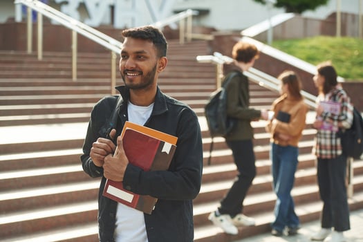 Man, with education materials in hands. Four young students in casual clothes are together outdoors photo