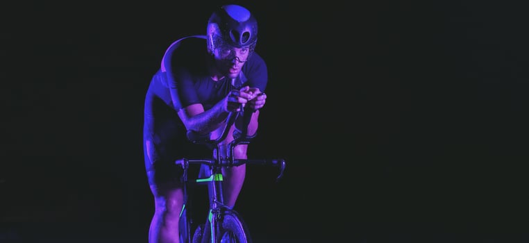 A triathlete rides his bike in the darkness of night, pushing himself to prepare for a marathon. The contrast between the darkness and the light of his bike creates a sense of drama and highlights the photo