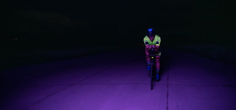 A triathlete rides his bike in the darkness of night, pushing himself to prepare for a marathon. The contrast between the darkness and the light of his bike creates a sense of drama and highlights the photo