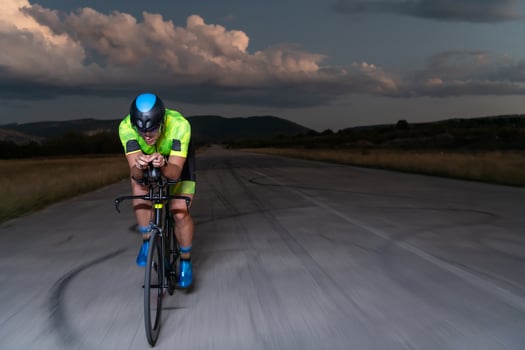 A triathlete rides his bike in the darkness of night, pushing himself to prepare for a marathon. The contrast between the darkness and the light of his bike creates a sense of drama and highlights the photo
