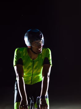 A triathlete rides his bike in the darkness of night, pushing himself to prepare for a marathon. The contrast between the darkness and the light of his bike creates a sense of drama and highlights the photo