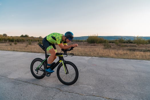 Triathlete riding his bicycle during sunset, preparing for a marathon. The warm colors of the sky provide a beautiful backdrop for his determined and focused effort. photo