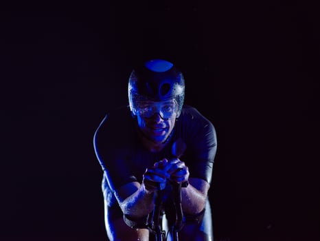 A triathlete rides his bike in the darkness of night, pushing himself to prepare for a marathon. The contrast between the darkness and the light of his bike creates a sense of drama and highlights the photo