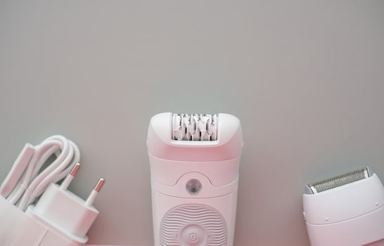 Modern electric epilator set with attachments and charging cable on pastel background photo