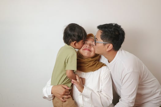 Asian Muslim mom dad embrace and kiss son sitting on sofa in living room photo