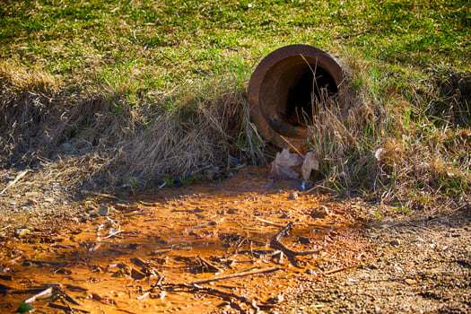 Polluted Water Flowing From a Rusty Drain Pipe Into Contaminated Soil in a Natural Environment photo
