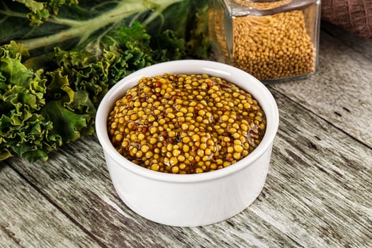 A bowl of mustard on a table next to a bunch of kale photo