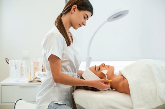 Lying ,down. Using brushes. Woman face getting facial care by beautician hands at spa salon photo