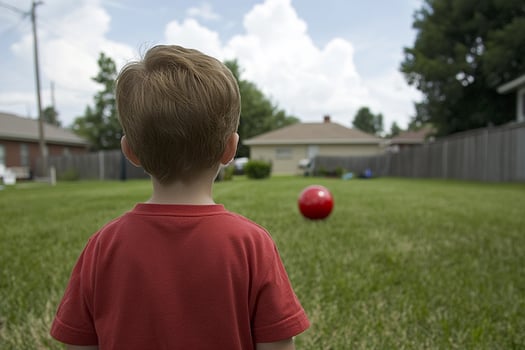 A young boy standing in a yard with a red ball photo