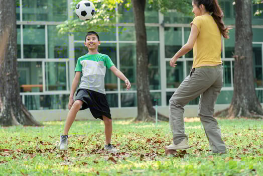 Fun and Bonding Through Soccer. A young boy joyfully plays soccer in the park with his mom. photo