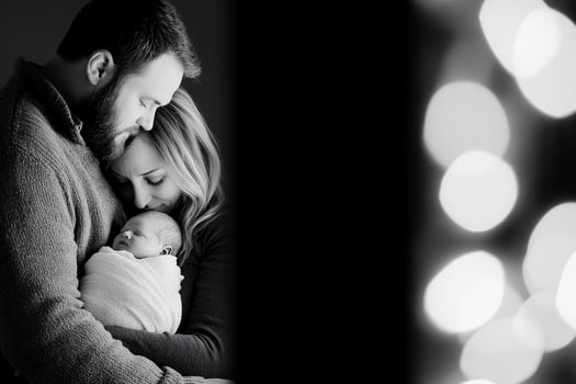 A couple holding their newborn in front of a black and white photo