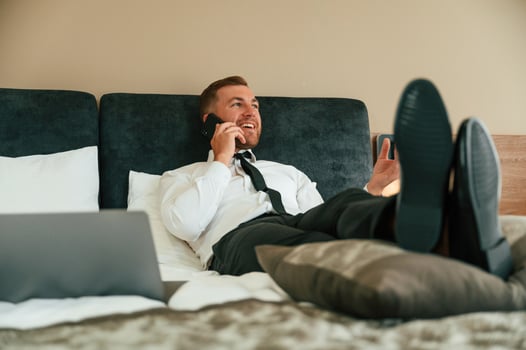 Having fun by ,talking by phone and lying down on bed. Businessman is indoors in the hotel room photo