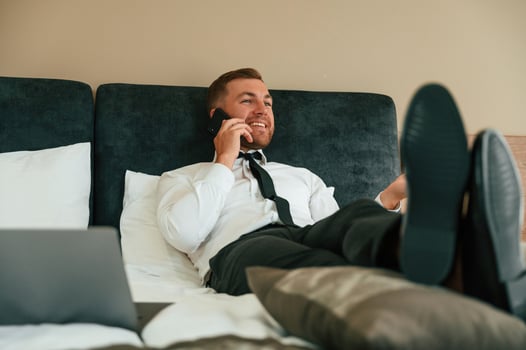 Smiling, lying ,down on bed and talking by phone. Businessman is indoors in the hotel room photo
