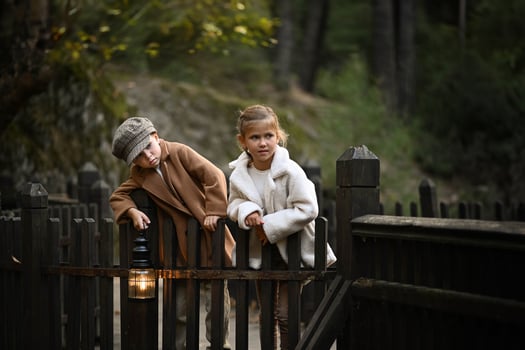 Captured in warm light, a little boy and girl share a quiet moment on a rustic wooden bridge. With a basket of baguettes and a vintage lantern beside them, the scene evokes the innocence of childhood. photo