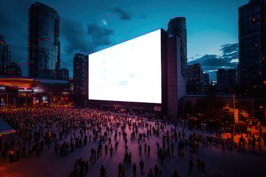 Large crowd of people gathering near a big blank screen in a city. Tall buildings and dark sky. Night cityscape with many silhouettes. photo