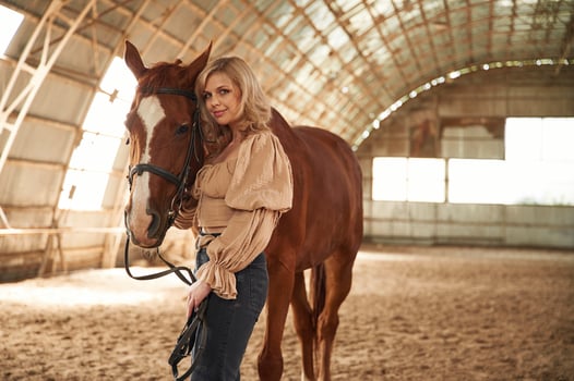 Sunny, day. Standing,with animal. Beautiful young woman is with horse indoors photo