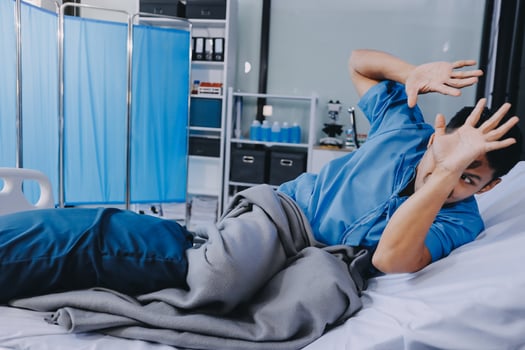 A man laying in a hospital bed with his hands up photo