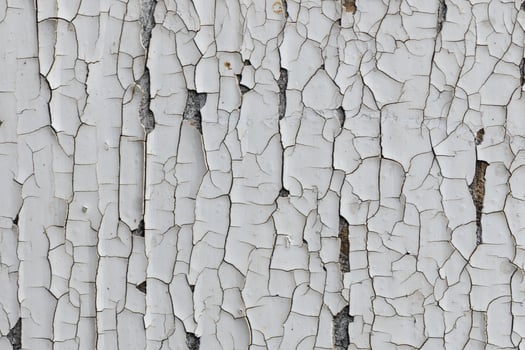 Weathered white paint revealing cracked texture on an aging wall surface in a forgotten urban setting photo