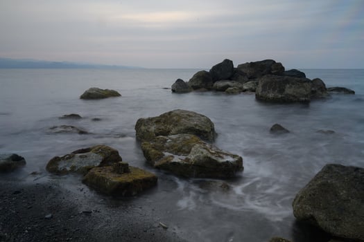 Serene twilight enveloping rocky shoreline with gentle waves lapping against ancient stones near a tranquil coastal retreat photo