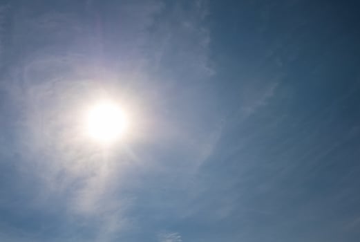 Bright sun shining through wispy clouds in blue sky photo