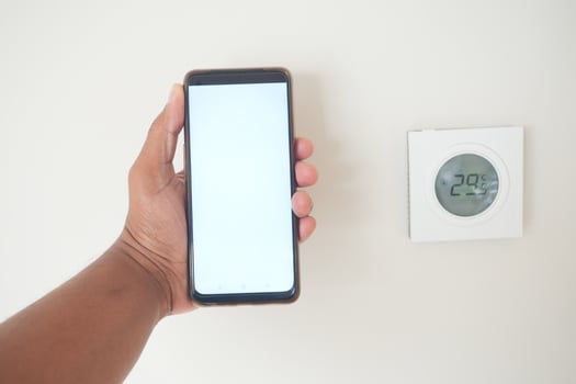 Hand holding smartphone next to digital thermostat showing temperature photo