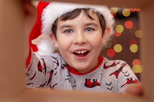 A surprised handsome boy in a Santa Claus hat takes a present out of the box photo