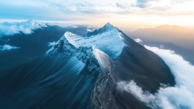 Aerial view of snow covered mountain peak surrounded by misty clouds at sunrise photo