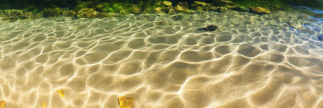 Sunlit waters with ripple patterns on clear shallow riverbed and rocks photo