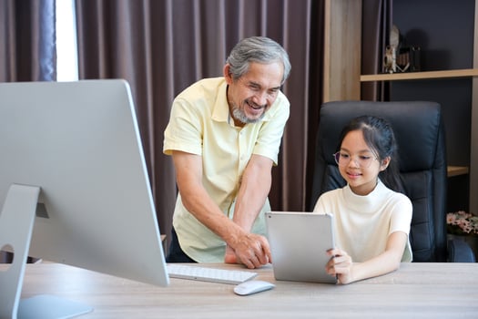 Young asian schoolgirl is doing her school homework assignment at home with advice from grandfather for education and study photo