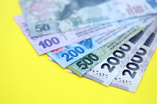Argentine pesos money bills lies on yellow color table close up photo