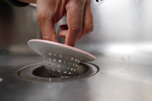 Kitchen hand placing a sink strainer into a drain for cleanup photo