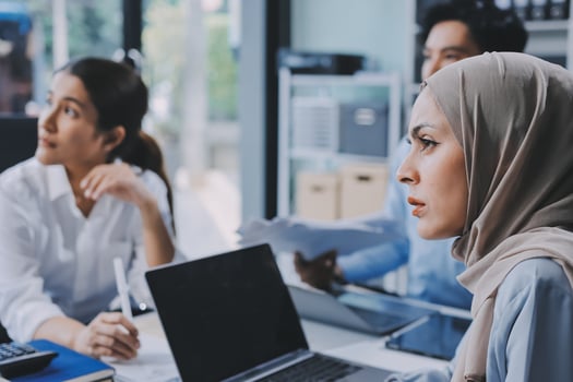 A woman wearing a hijab is sitting at a desk with two other people photo