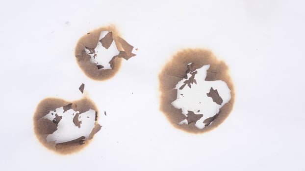 Three burned holes on a white paper isolated on white background photo